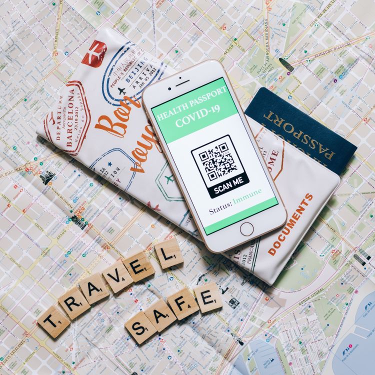 A photo of a map with scrabble letters on it that spell out travel safe.  The photo also includes a smartphone and a passport.